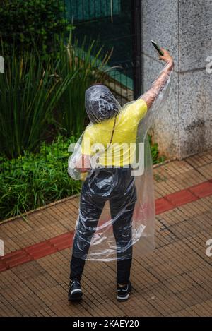 Femme portant un poncho de pluie jetable prenant un selfie à Belo Horizonte, Brésil. Banque D'Images