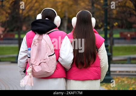 Deux filles dans les mêmes vêtements et casques marche dans une rue de ville. Lits jumeaux dans le parc d'automne Banque D'Images