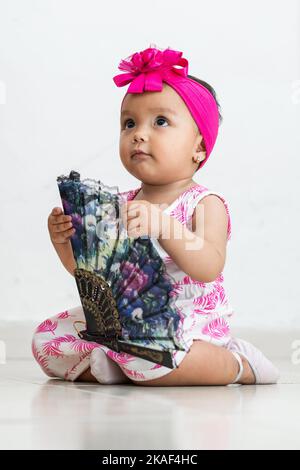 brunette bébé assis sur le sol avec un ventilateur dans ses mains tout en regardant vers le haut. fond blanc Banque D'Images