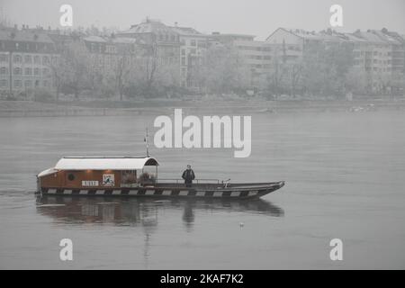 Un homme sur un bateau naviguant dans le Rhin près de la rive lors d'une matinée d'hiver brumeuse à Bâle, Suisse Banque D'Images