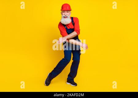 Photo de funky gai âge homme vêtements de travail général Red Hat danse ayant un arrière-plan isolé couleur jaune Banque D'Images