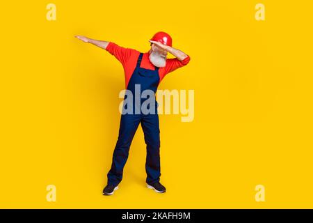 Photo de gai positif l'âge homme vêtements de travail général rouge casque de danse ayant amusant isolé couleur jaune fond Banque D'Images