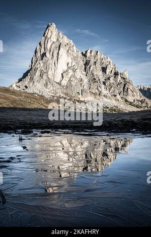 La face rocheuse du Mont Ragusela se reflète dans l'eau et la glace d'un étang lors d'une matinée d'automne glacielle à Passo di Giau, Dolomites, Italie Banque D'Images