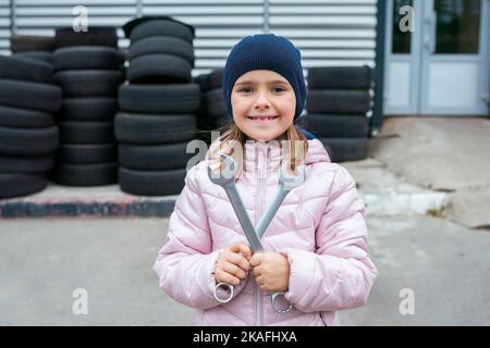 Portrait d'un enfant heureux avec des clés contre l'arrière-plan d'un garage et des pneus de roue et l'entretien de véhicule. Concept de réparation automatique Banque D'Images