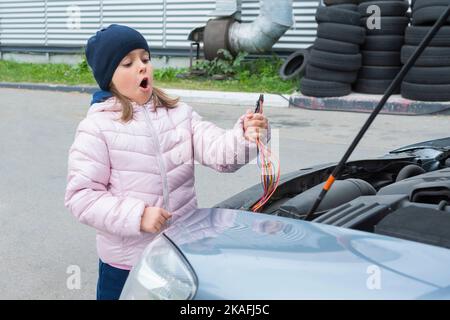 Un mécanicien d'enfant répare une batterie dans une voiture. Réparation de voiture Banque D'Images