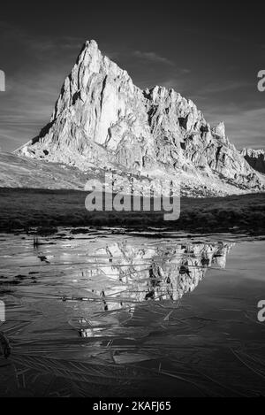 La face rocheuse du Mont Ragusela se reflète dans l'eau et la glace d'un étang lors d'une matinée d'automne glacielle à Passo di Giau, Dolomites, Italie Banque D'Images