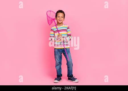 Photo pleine grandeur de gai drôle optimiste garçon habillé rayé chemise Jean tenant le filet de papillon isolé sur fond de couleur rose Banque D'Images