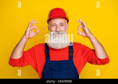 Photo de funky positif âge homme vêtements de travail général Red Hat montrant deux gestes clés isolé couleur jaune arrière-plan Banque D'Images