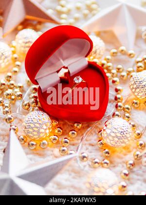 Décorations étoiles de Noël et du nouvel an sur fond blanc tricoté. Boîte cadeau cœur rouge avec bague dorée et ampoules métalliques Banque D'Images