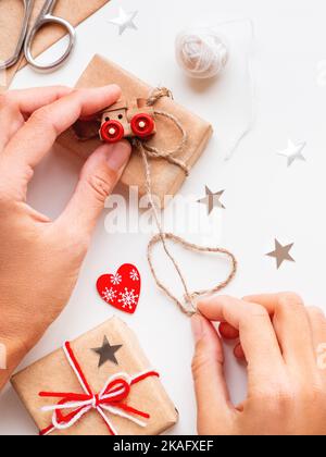 Femme emballage bricolage présente en papier artisanal. Cadeaux liés avec des fils blancs et rouges avec jouet train comme décoration. Banque D'Images