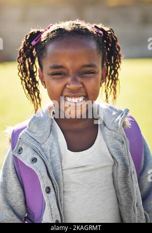 Son sourire peut égayer n'importe quel jour. Portrait d'une fille de l'école élémentaire debout à l'extérieur. Banque D'Images