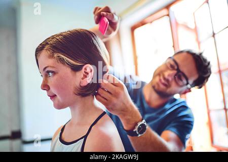 HES est vraiment impliqué dans chaque partie de sa vie. Un père peignant ses petites filles cheveux à la maison. Banque D'Images