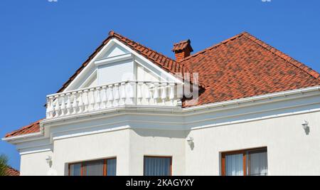 Maison de luxe moderne avec mur blanc, lumières extérieures, balcon, gouttière, toit en céramique et volets roulants de fenêtres mansardées. Banque D'Images