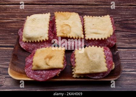 Gnocco Fritto avec salami sur une table rustique en bois. Succédanés italiens de pain fait avec de la pâte frite. Banque D'Images