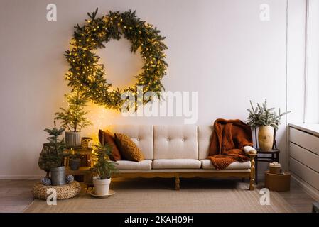 Intérieur de Noël confortable du salon avec un canapé, arbres de Noël et une couronne sur le mur avec des lumières Banque D'Images