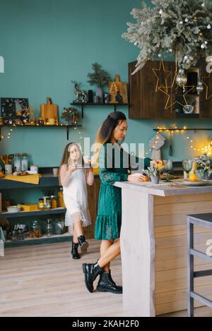 La jeune mère et la petite fille regardent une tarte aux baies fraîchement cuite dans une cuisine de Noël décorée. Le concept des traditions familiales Banque D'Images