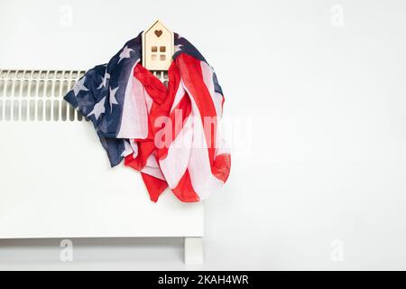 Une petite maison en bois et le drapeau de l'Amérique se trouve sur un convecteur de chauffage sur fond blanc, une maison chaude en Amérique, la saison de chauffage Banque D'Images