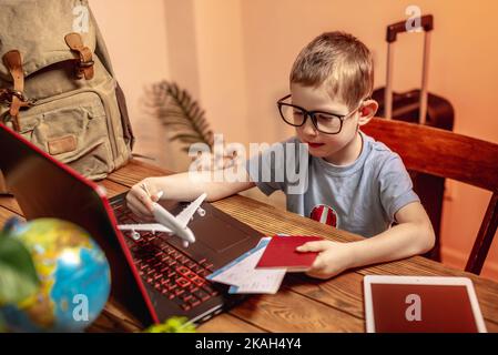 Un enfant achète des billets d'avion pour un ordinateur portable en ligne à la maison. Voyager est facile, même un enfant peut le manipuler. Banque D'Images