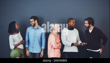 Il y a tellement de choses à discuter. Photo en studio d'un groupe diversifié de personnes debout et discutant sur fond gris. Banque D'Images