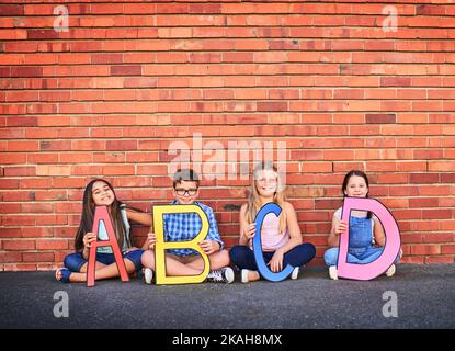 L'éducation ouvre l'esprit. Portrait d'un groupe de jeunes enfants tenant des lettres de l'alphabet contre un mur de briques. Banque D'Images