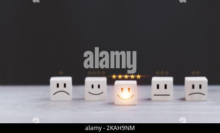 le service clientèle est la meilleure expérience de notation professionnelle. Concept d'enquête de satisfaction. Main d'un homme d'affaires choisit une smiley visage sur le bloc de bois cu Banque D'Images