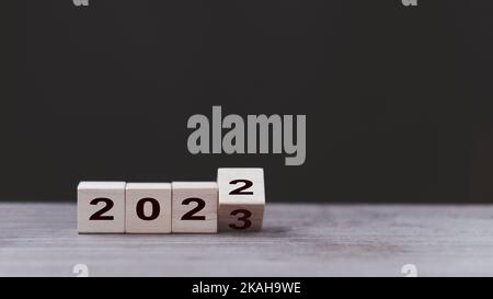 2023 bannière du concept de la bonne année. Retourner le calendrier des numéros de 2022 à 2023 ans sur des blocs de cube en bois isolés sur fond sombre pour le nouvel an cha Banque D'Images