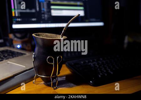Le soir, prenez un verre au travail. Un maté de calabas au premier plan. En arrière-plan des ordinateurs et un moniteur. Travailler et boire yerba mate. Banque D'Images
