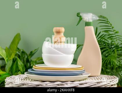 Lavage de vaisselle écologique. Un style de vie sans gaspillage. Spray lave-vaisselle avec pile de plaques en céramique avec brosse à vaisselle en bambou de sisal sur fond vert Banque D'Images