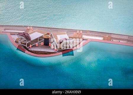 L'été amour et romance table pour un dîner romantique avec chaises longues à débordement de piscine sous le ciel de coucher de soleil et la mer en arrière-plan. Luxe Banque D'Images