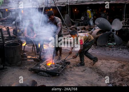 Un employé jette des pigees métalliques dans le four pour les faire fondre. L'industrie de la construction navale au Bangladesh se répand rapidement là où les travailleurs de tous âges travaillent ensemble, à Dhaka, au Bangladesh, sur 28 avril 2016. Les conditions de travail sont graves et ne conviennent pas aux enfants. Les conditions sont chaudes et souvent dangereuses. Même les travailleurs n'utilisent pas de protection minimale. Par conséquent, les accidents se produisent très fréquemment. Les enfants qui travaillent ici grandissent sans éducation, ce qui les a menés vers un avenir incertain. La raison du travail des enfants dans de telles conditions de travail dangereuses est le travail bon marché et la pauvreté Banque D'Images