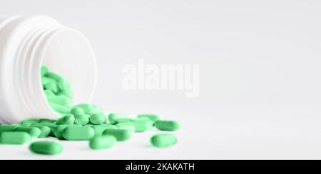 Pilules vertes avec renversé hors d'un pot en plastique. Capsules de médicaments sur fond blanc avec espace de copie. Banque D'Images