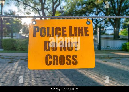 La ligne de police ne croissera pas le panneau d'affichage jaune suspendu sur une corde vue rapprochée. Signalisation d'avertissement empêchant l'entrée dans la route, la clôture, les arbres et le bâtiment Banque D'Images
