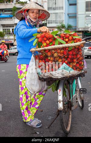 Femme vietnamienne, motard, portant un chapeau de bambou, vendant un ramboutan à partir d'une bicyclette dans le centre de Ho Chi Minh ville, Vietnam Banque D'Images