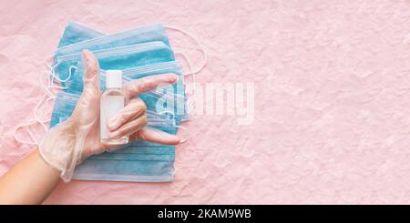 Vue de dessus à portée de main dans des gants de protection avec masques médicaux et assainisseur dans un flacon transparent. Femme fait le geste de victoire. Concept de coronavirus COVID-19 Banque D'Images