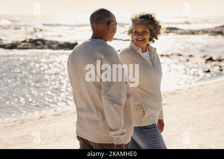 Joyeux couple de personnes âgées souriant les uns les autres tout en faisant une promenade le long de la plage. Couple senior romantique passant un moment de qualité ensemble après la ré Banque D'Images