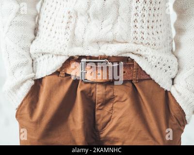 Femme en pull blanc à maille torsadée avec motif scandinave et pantalon chino marron avec ceinture en cuir. Vêtements décontractés pour un temps de détente. Ur. Moderne Banque D'Images