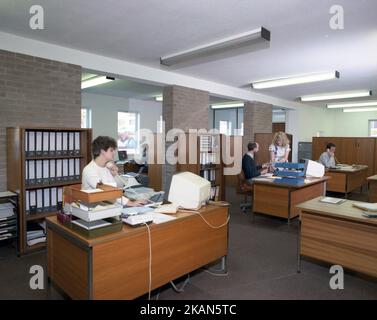 1989, personnel historique, masculin et féminin travaillant dans un bureau, assis à des bureaux en bois, avec dans des plateaux, ajoutant des machines et de petits terminaux d'ordinateur du jour. Banque D'Images