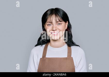 Jeune femme en tablier, regardant la caméra sur fond gris Banque D'Images