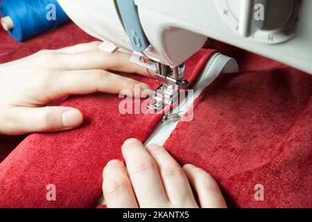 couturière les mains cousues sur la fermeture à glissière sur l'article rouge de vêtements par machine à coudre moderne avec le pied de presse spécial. processus de couture Banque D'Images