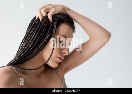 Portrait de jeune femme tatouée avec des tresses touchant les cheveux isolés sur gris, image de stock Banque D'Images