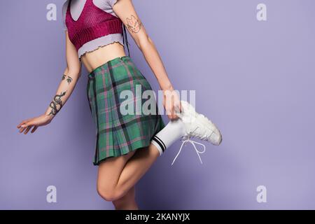 vue rognée de la femme tatouée en jupe à carreaux réglage sneaker blanche sur fond violet, image de stock Banque D'Images