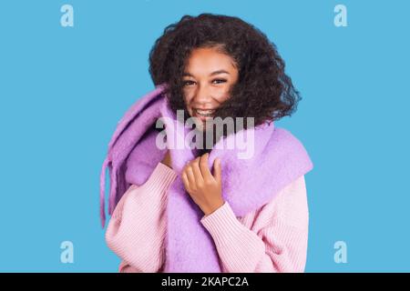 Une photo en gros plan d'une jolie femme souriante vêque de vêtements d'hiver roses et violets, isolés sur fond cyan Banque D'Images