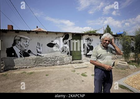 Krustyo Tonev rit alors qu'il se tient devant les peintures murales de sa maison représentant le président américain Donald Trump, chancelier de l'Allemagne, Anglea Merkel dans le cadre du Festival mural dans le village de Staro Zhelezare, Bulgarie, mercredi 26 juillet 2017. Les peintures murales extérieures sur les murs des maisons du village de Staro Zhelezare présentent des gens locaux ainsi que des figures bien connues des mondes de la politique et de la religion. (Photo de Valentina Petrova/NurPhoto) *** Veuillez utiliser le crédit du champ de crédit *** Banque D'Images