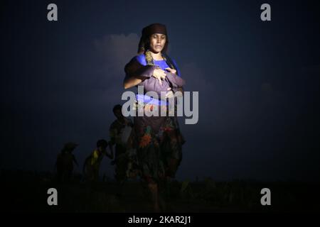 Une femme de Rohingya porte son enfant tout en marchant dans un champ de riz après avoir traversé la frontière avec le Bangladesh près de Cox's Bazar, Teknaf, Bangladesh sur 5 septembre 2017. Au total, 87 000 réfugiés, pour la plupart des Rohingya, sont arrivés au Bangladesh depuis que la violence a éclaté au Myanmar voisin sur le 25 août, ont déclaré aujourd'hui les Nations Unies, dans le contexte des critiques internationales croissantes à l'encontre d'Aung San Suu Kyi. Environ 20 000 autres ont été massés à la frontière en attendant d'entrer, a déclaré l'ONU dans un rapport. (Photo par Mushfiqul Alam/NurPhoto) Banque D'Images