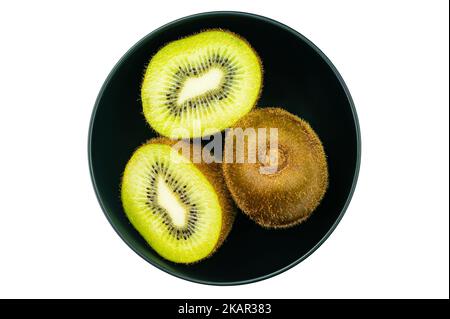 Vue de dessus, plat de kiwis frais mûrs, kiwis dans un bol en céramique noir entier et deux moitiés isolées sur fond blanc avec un piton à cheveux Banque D'Images