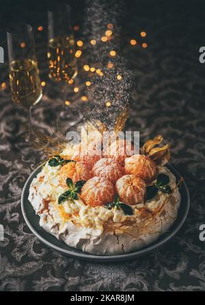 Pavlova gâteau basse lumière encore vie verser avec sucre en poudre à base de meringue dessert nommé d'après la ballerine russe décorée avec des mandarines fraîches, c Banque D'Images