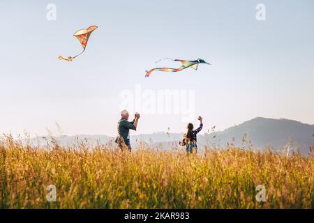 Un père souriant avec sa fille qui libère des cerfs-volants colorés sur la prairie haute herbe. Profitez en famille de moments photo d'été ou de temps en extérieur Banque D'Images