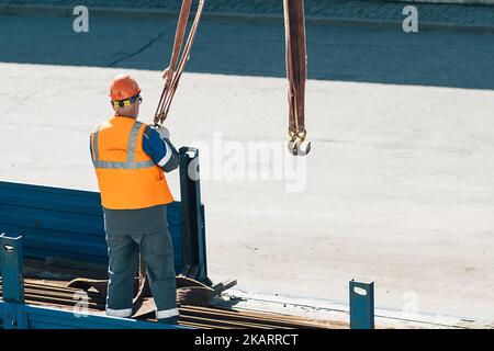 Le déflecteur du casque et de la veste décharge les tuyaux et raccords métalliques de la caisse du camion par temps clair. Arrière-plan de production. Flux de travail authentique sur site de construction. Le déflecteur au travail. Banque D'Images