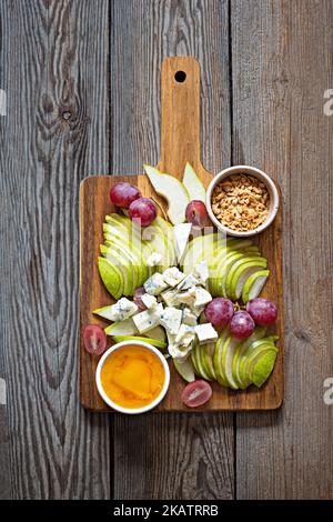 Tranches de fromage bleu, de bleu ou de roquefort et fruits (raisins, poires), noix et miel sur une planche. Hors-d'œuvre exquis pour le vin. Assiette de fromages fruités. Banque D'Images