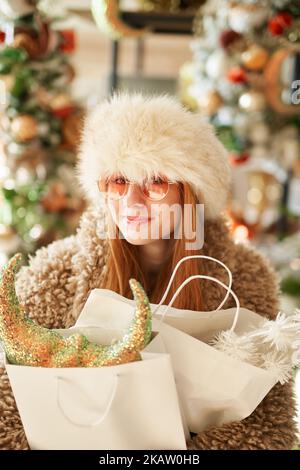 Jolie petite fille caucasienne dans des vêtements chauds d'extérieur et des lunettes de soleil avec des sacs de shopping plein de décoration de Noël dans le magasin ou le centre commercial. Thème shopping ou consumérisme de la nouvelle année Banque D'Images